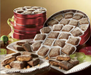 Three sizes of red tins of butter toffee, with a tipped tin allowing some toffee to flow onto decorative plates.