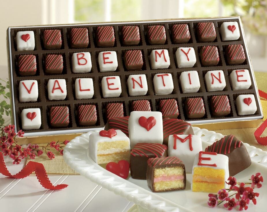 Red striped chocolate petits fours that reads be my valentine, coated with white chocolate and red hearts.