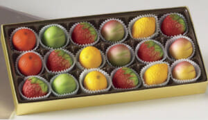 Marzipan candy in the shapes of strawberries, lemons, oranges, peaches and green apples nestled in a gold box.