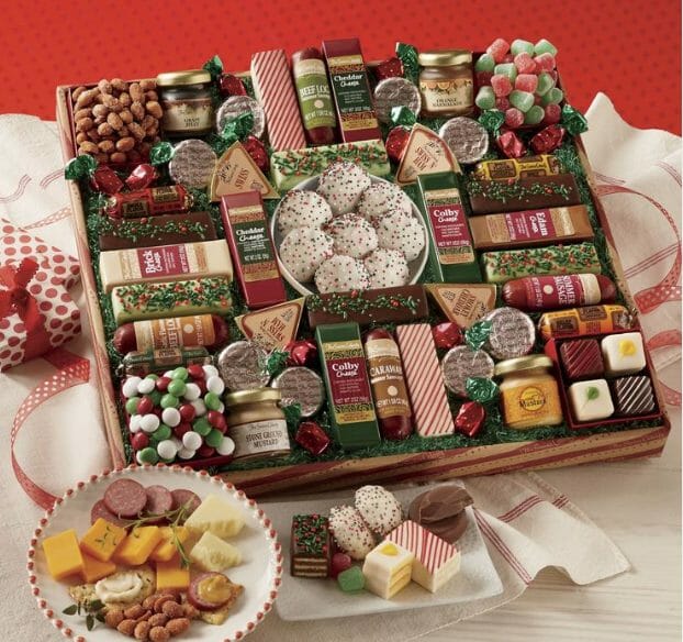 Holiday food gift box of snack size cheese, sausage, desserts, nuts, mustards and candies with a small plate of samples.