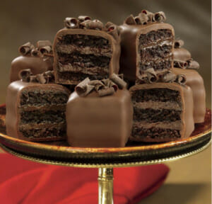 Hand decorated, layered chocolate petits fours with chocolate curls on top.