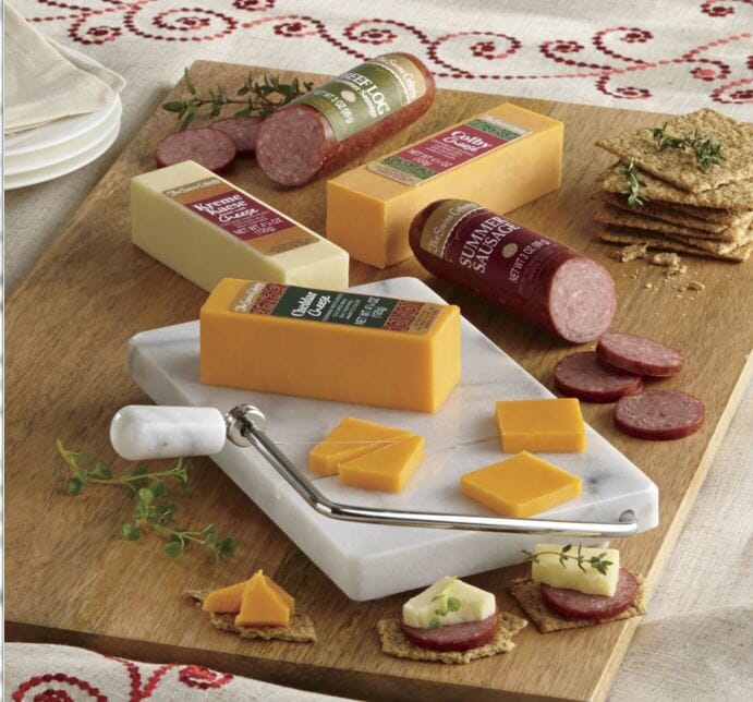 Cheese bars and beef logs with slices of cheese and sausage on a marble slicer, with crackers and appetizers.