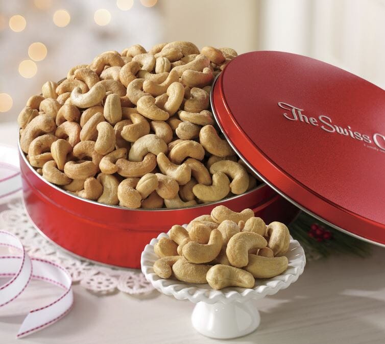 Jumbo Cashews in a red Swiss Colony tin, with a small pedestal plate filled with samples. 