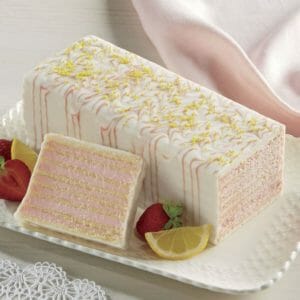Decorative pink and white dobosh torte on a white platter, with a slice displaying the many layers, and fruit garnish.