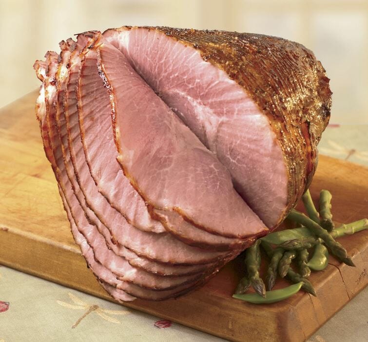 Honey glazed spiral ham and asparagus spears displayed on a chopping block.