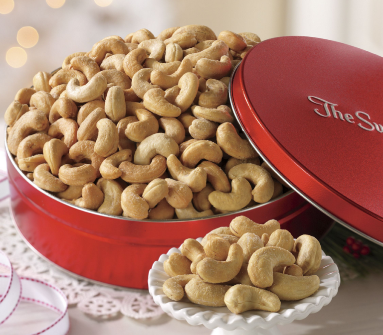 Jumbo cashews in an opened red tin with a filled sample size pedestal plate on the side.
