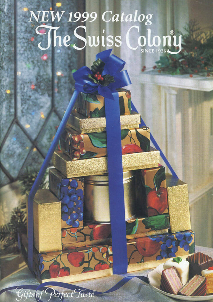 1999 Swiss Colony Catalog Cover - stack of food gifts in fruit on the vine gift boxes and blue ribbon.