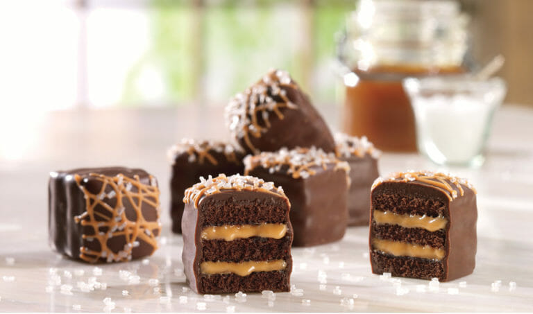 A close-up view of salted caramel petits fours, one cut to show the soft caramel filling.