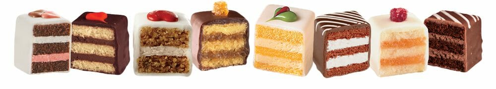 A row of eight petits fours in a variety of flavors, cut in half to display the layers.