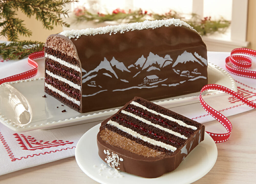 Layered chocolate dobosh torte with an alpine scene on the side, and a plate with a slice of the torte.
