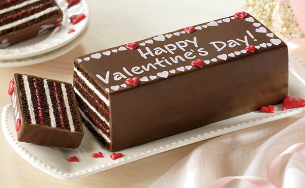 Chocolate torte with layers of cake, red and white filling, and happy valentine's day! written on top.