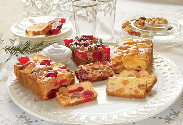 A trio of fruitcake bars displayed on a platter, cut to show the flavors of macadamia nut, butter rum and original.