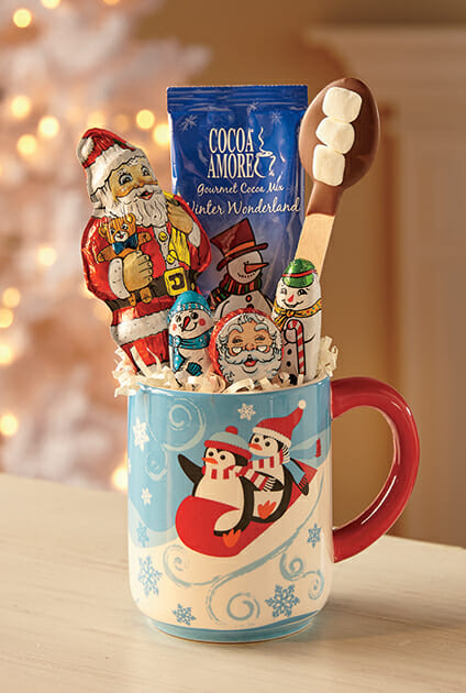 Chocolate candy gift in a winter penguin mug filled with cocoa mix, chocolates and a chocolate dipped spoon.