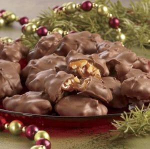 Chocolate caramel pecan clusters served on a red platter with holiday greenery and shiny garland.