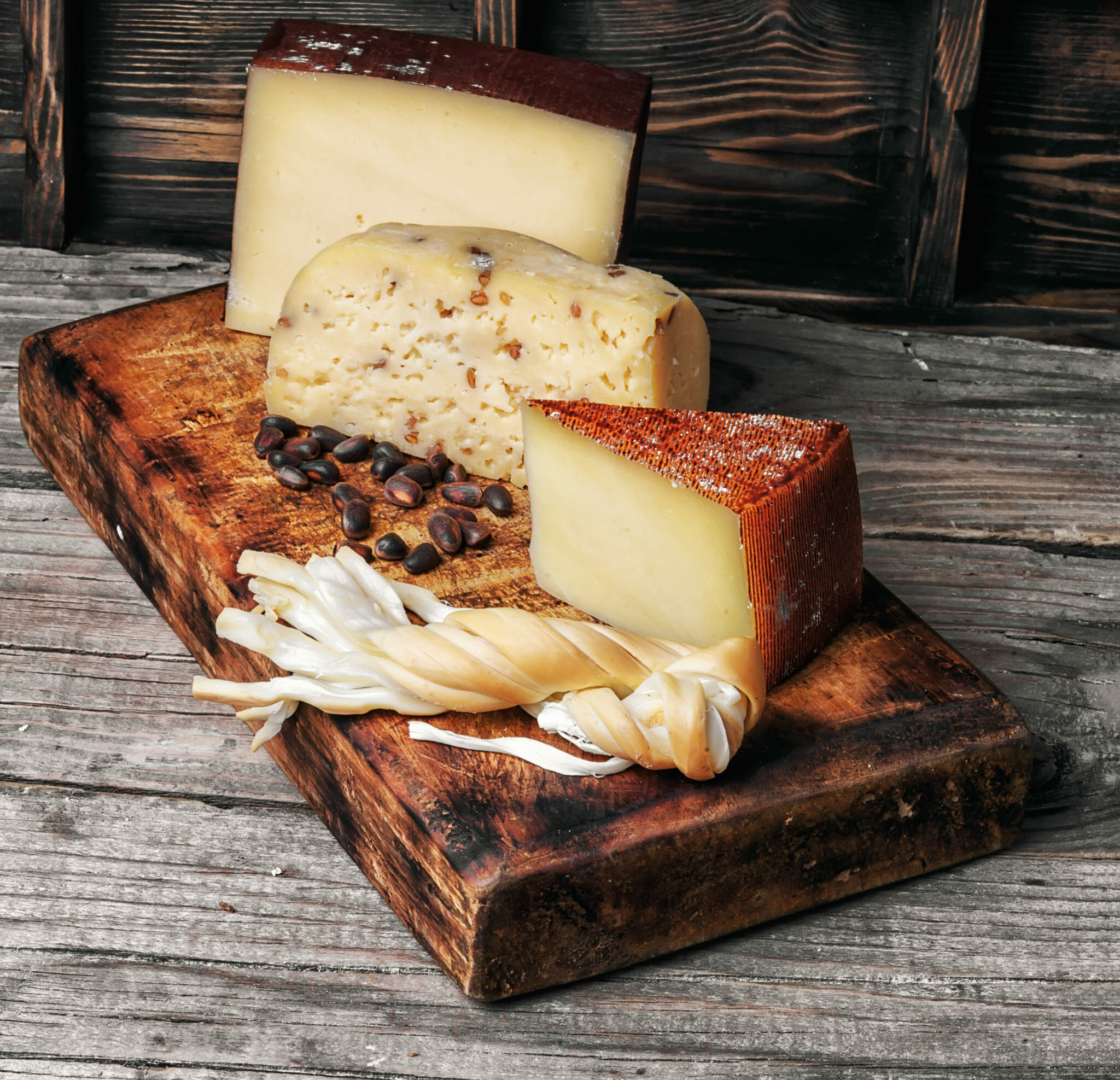 Range of three Swiss cheeses on a rustic, charred wooden cutting board.