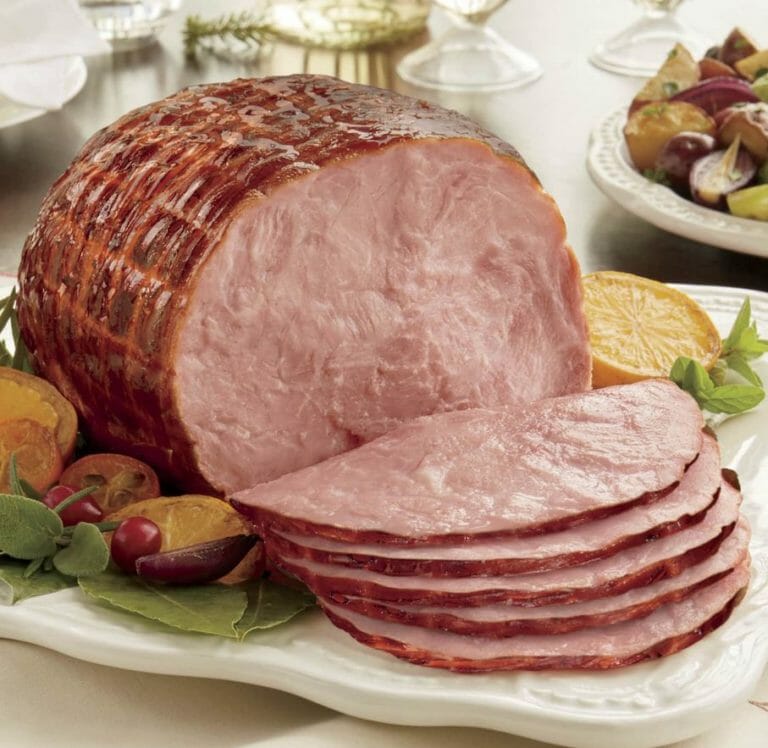 Boneless spiral ham and slices served on a white platter with grapes and sliced citrus fruit as garnish.