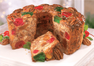 Christmas Fruitcake on a white platter, sliced to show the density of nuts and candied fruits inside.
