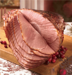 Honey glazed spiral ham and red cranberries displayed on a chopping block.