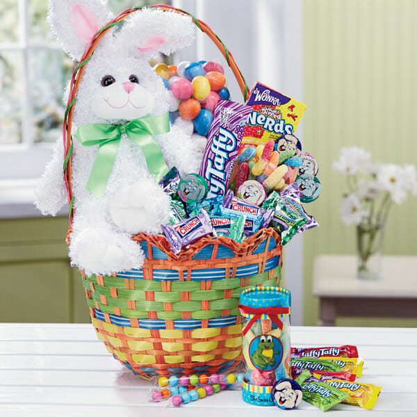 A colorful woven basket filled with a stuffed white bunny and a variety of Easter candy