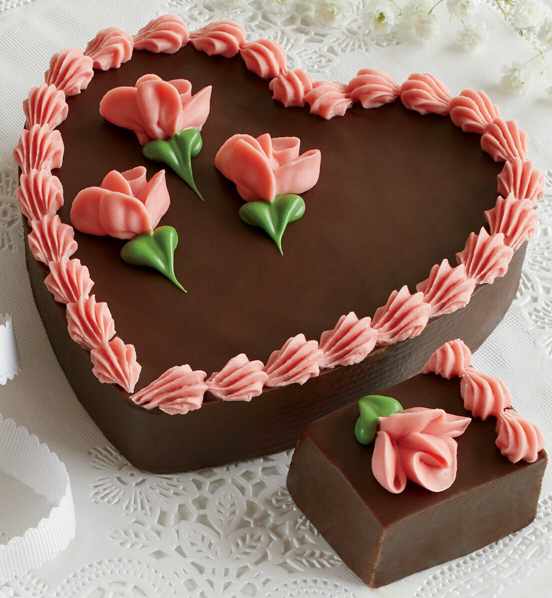 A large, heart-shaped block of fudge hand decorated with pink frosting roses and piping